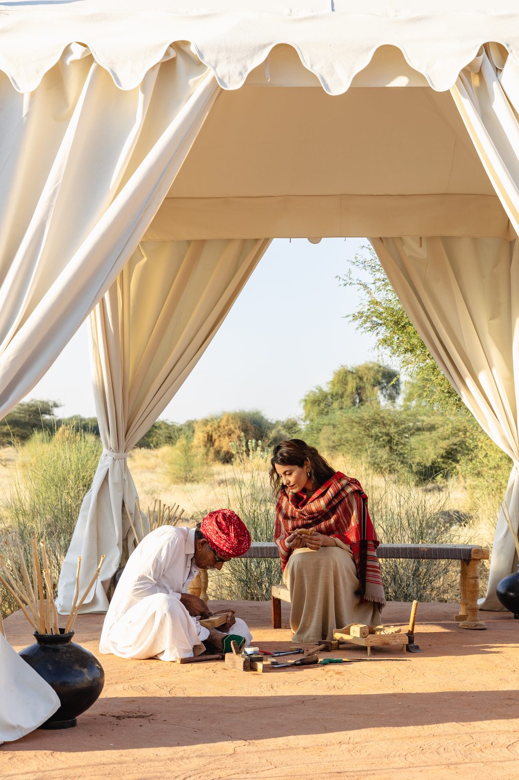 A craftsman teaching a guest traditional woodworking under a tented pavilion in the Rajasthan desert, Sujan The Serai