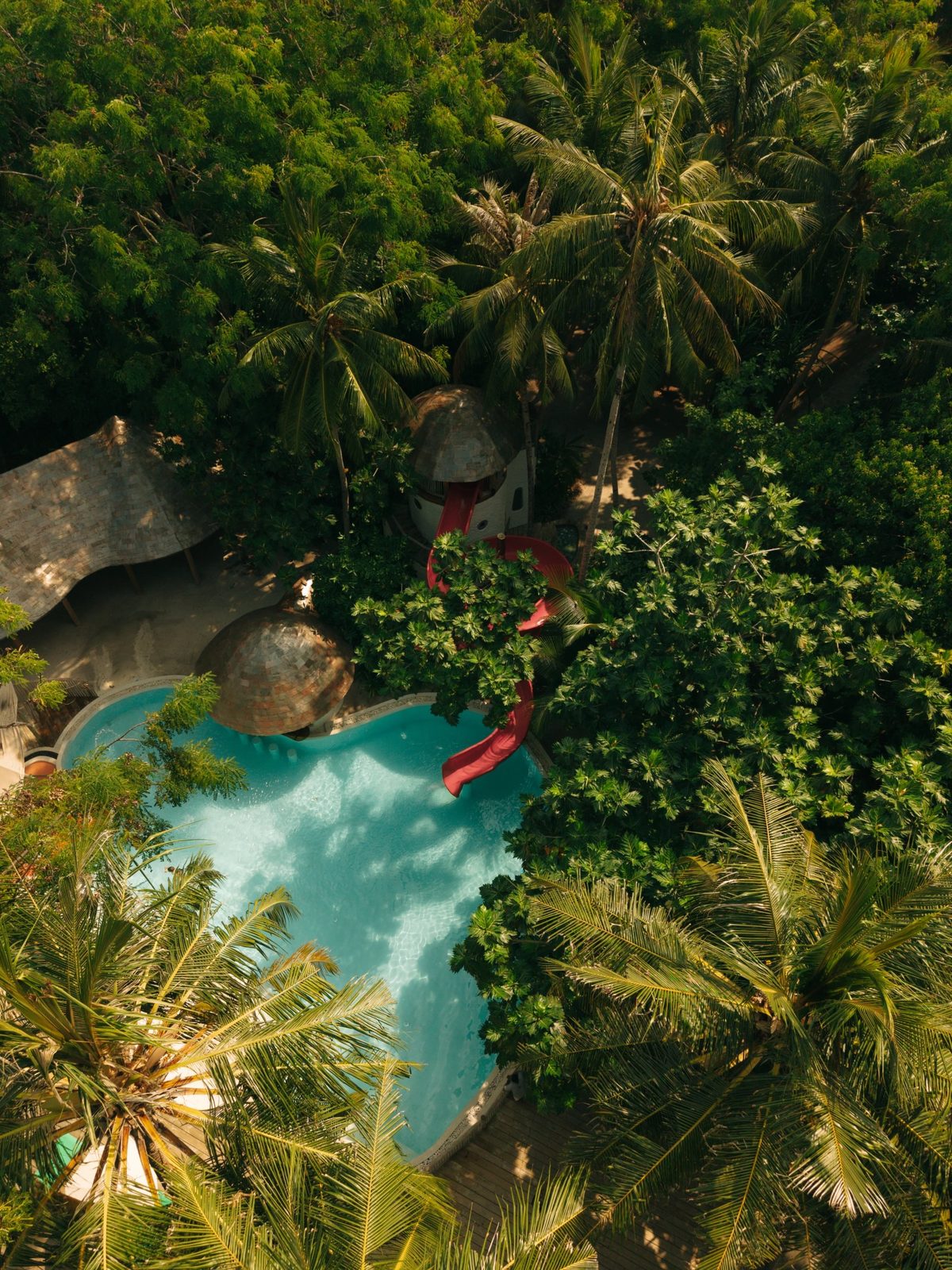 Aerial view of a lagoon pool with a red waterslide surrounded by palm trees at Soneva Fushi, Maldives