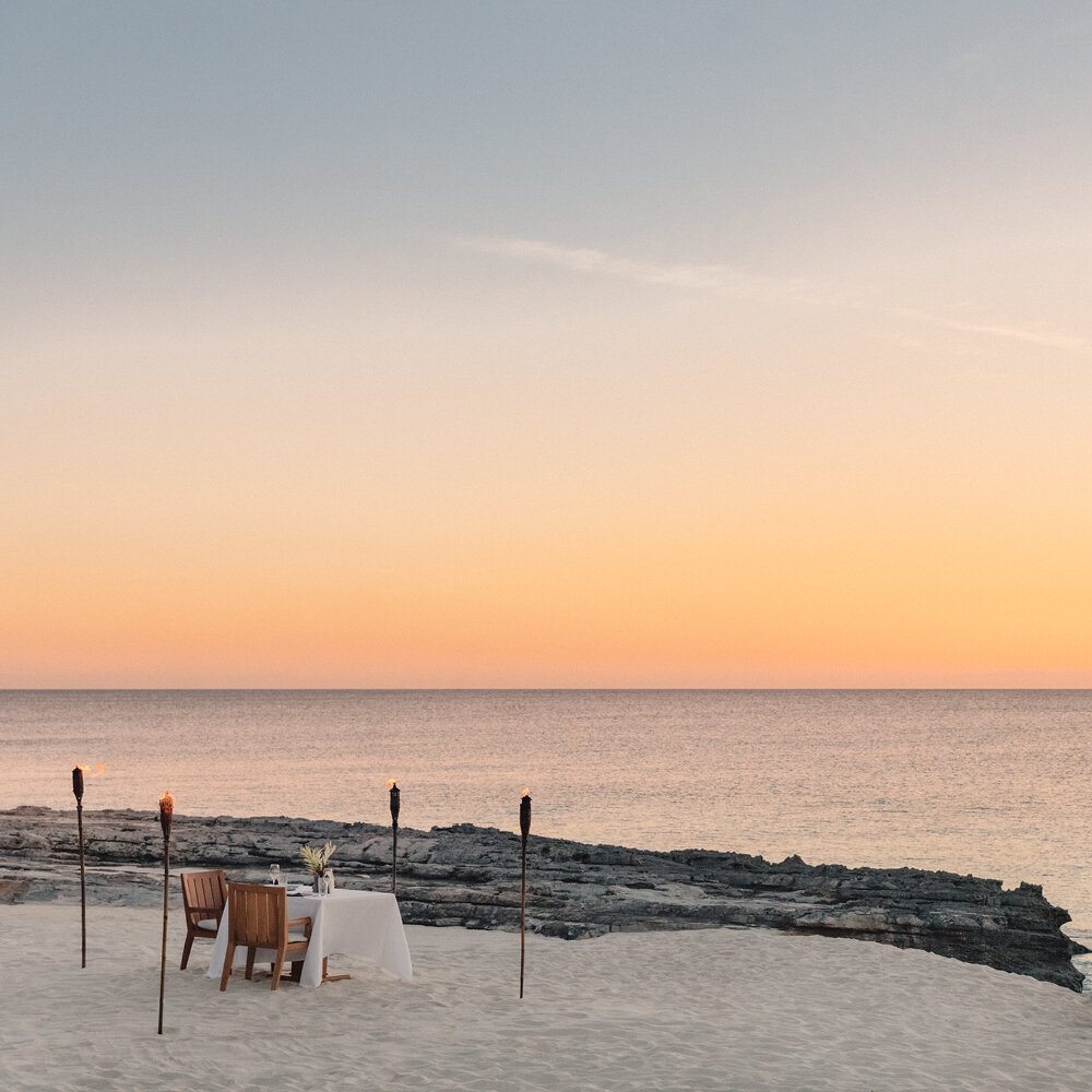 A private beachfront dinner table lit by torches at sunset, Aman Turks and Caicos