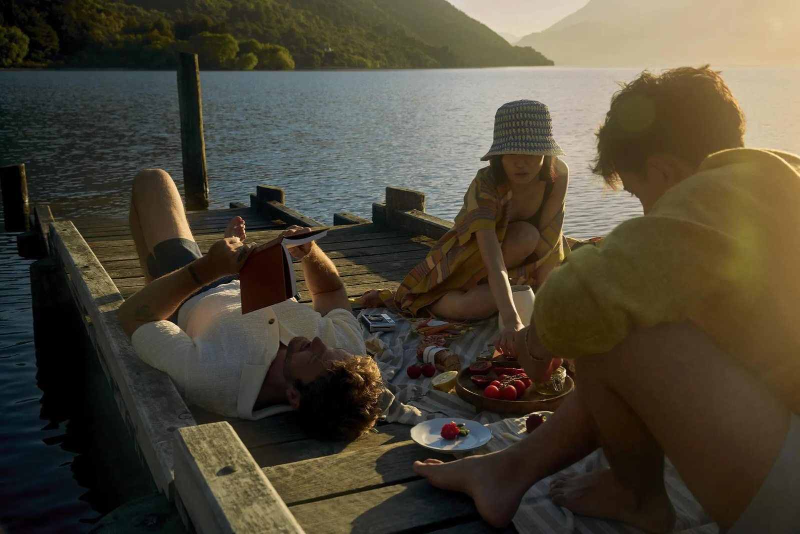 Friends picnicking on a lakeside dock at golden hour, Rosewood Matakauri, New Zealand