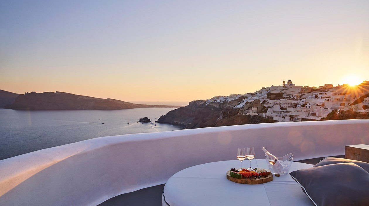 Private table set with wine and a cheese board overlooking the caldera and whitewashed town of Oia, Santorini