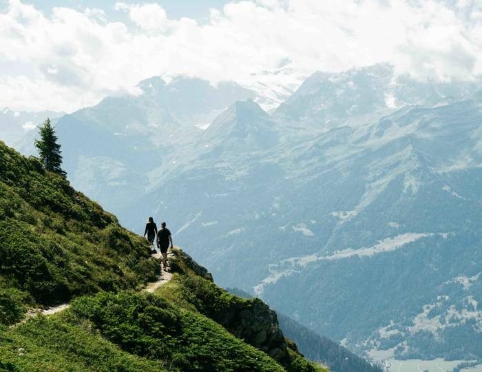 Two hikers walking a ridge trail above the Swiss Alps