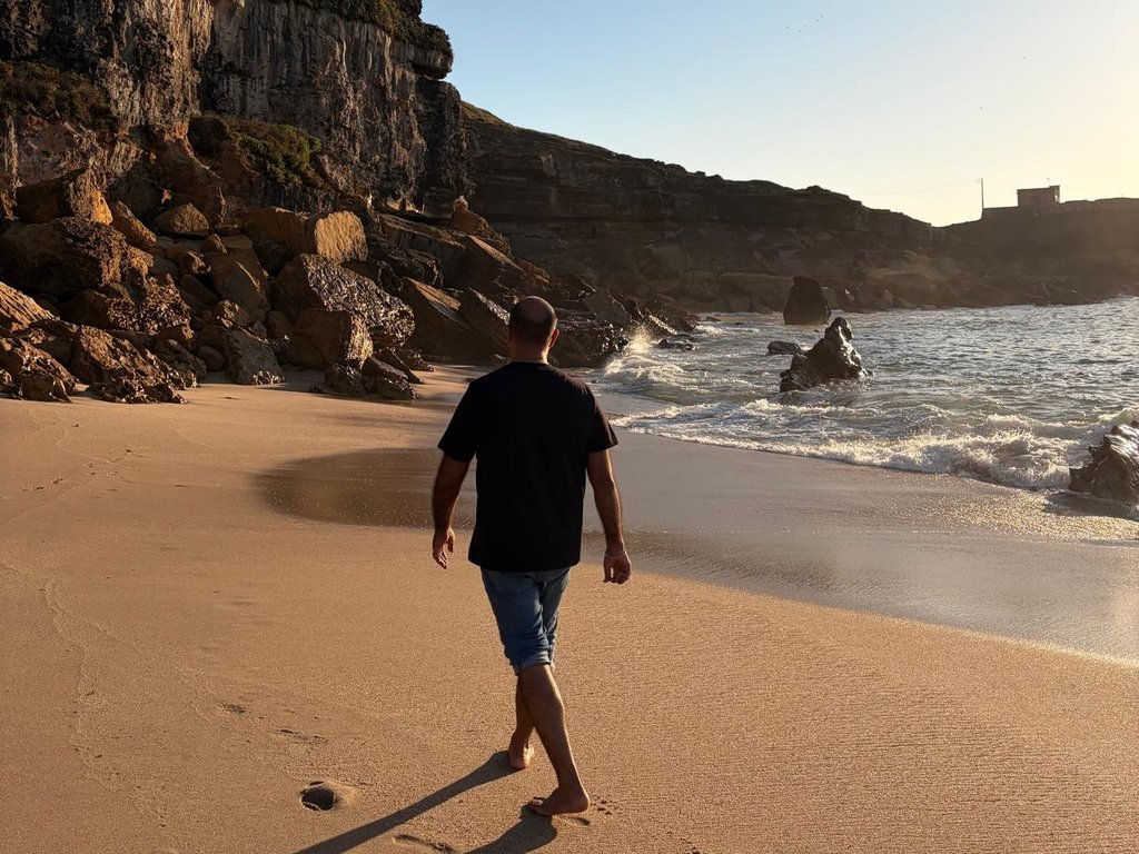 A man walking barefoot along a golden beach beneath tall cliffs