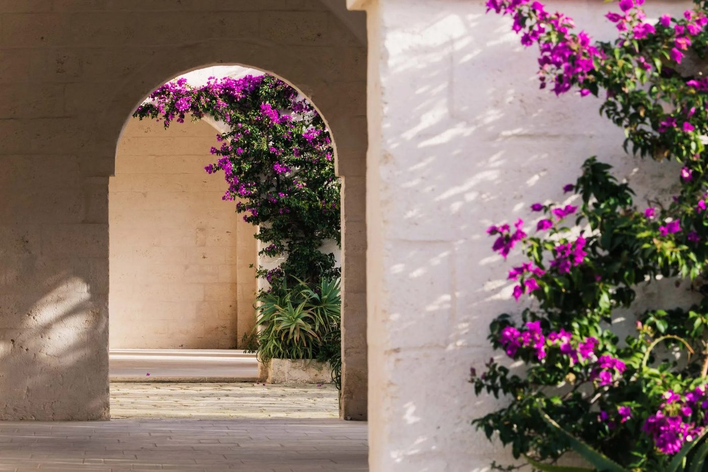 A sunlit stone archway framed by magenta bougainvillea at Borgo Egnazia, Puglia