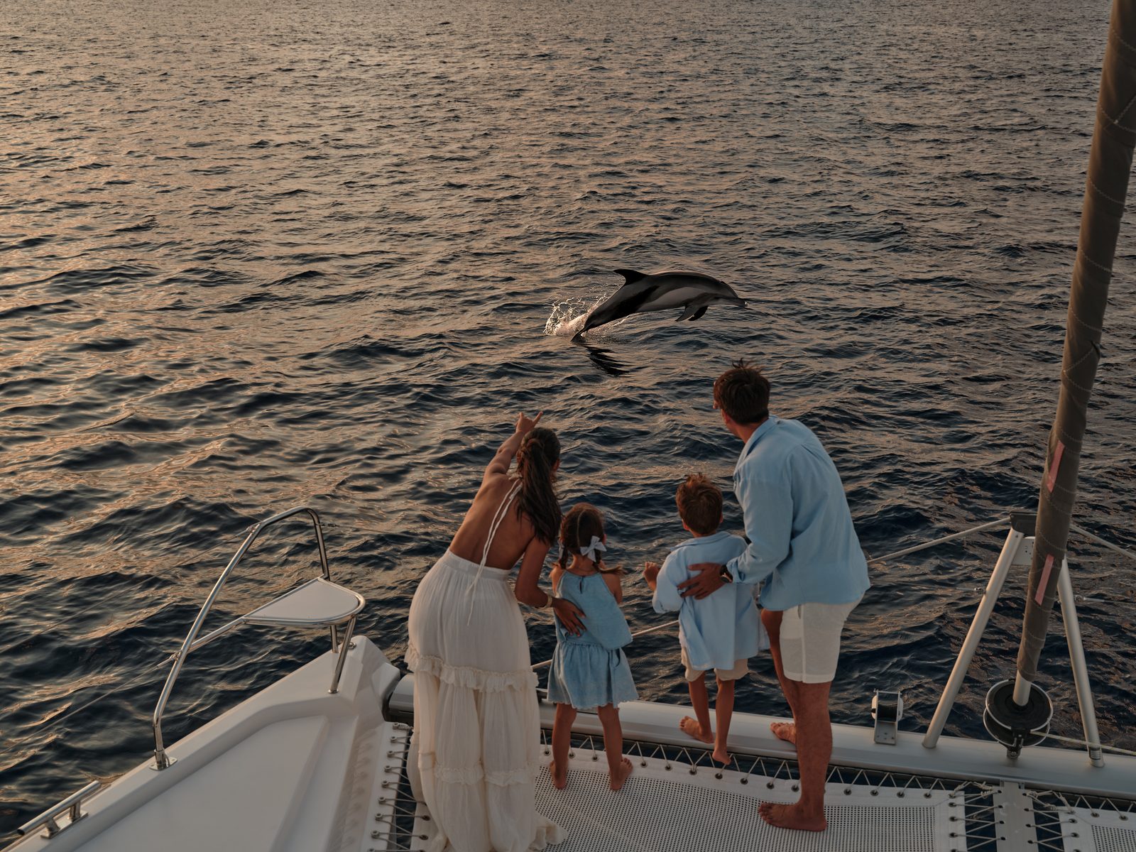 Family watching a dolphin leap beside their boat at sunset near Patina Maldives